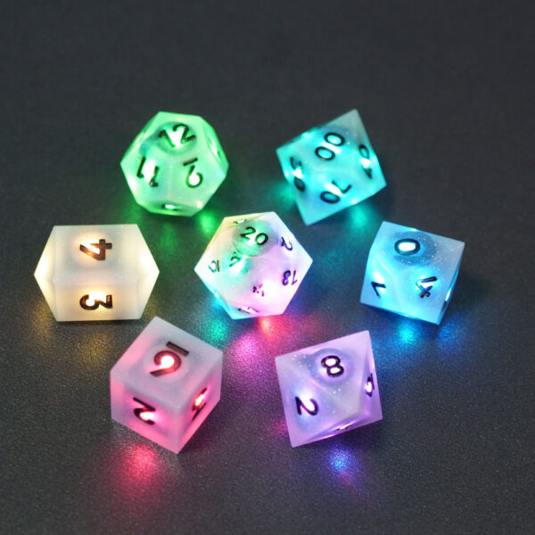 Set of 7 lit Aurora Sky dice with a rainbow of colors across all faces. Set Includes: 1 D20, 1 D12, 1 D00, 1 D10, 1 D8, 1 D6, 1 D4. Aurora Sky colorway is a mostly translucent white resin base packed with small blue and silver glitter throughout. The numbers or symbols are painted metallic black.